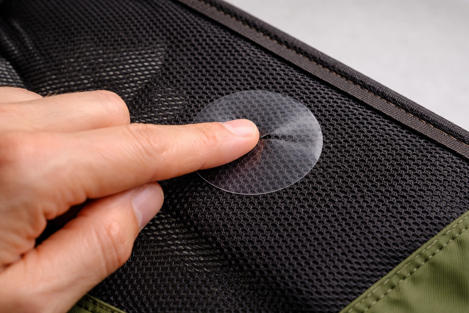 Close-up of hand pressing clear adhesive repair patch onto small tear in black mesh camping chair fabric
