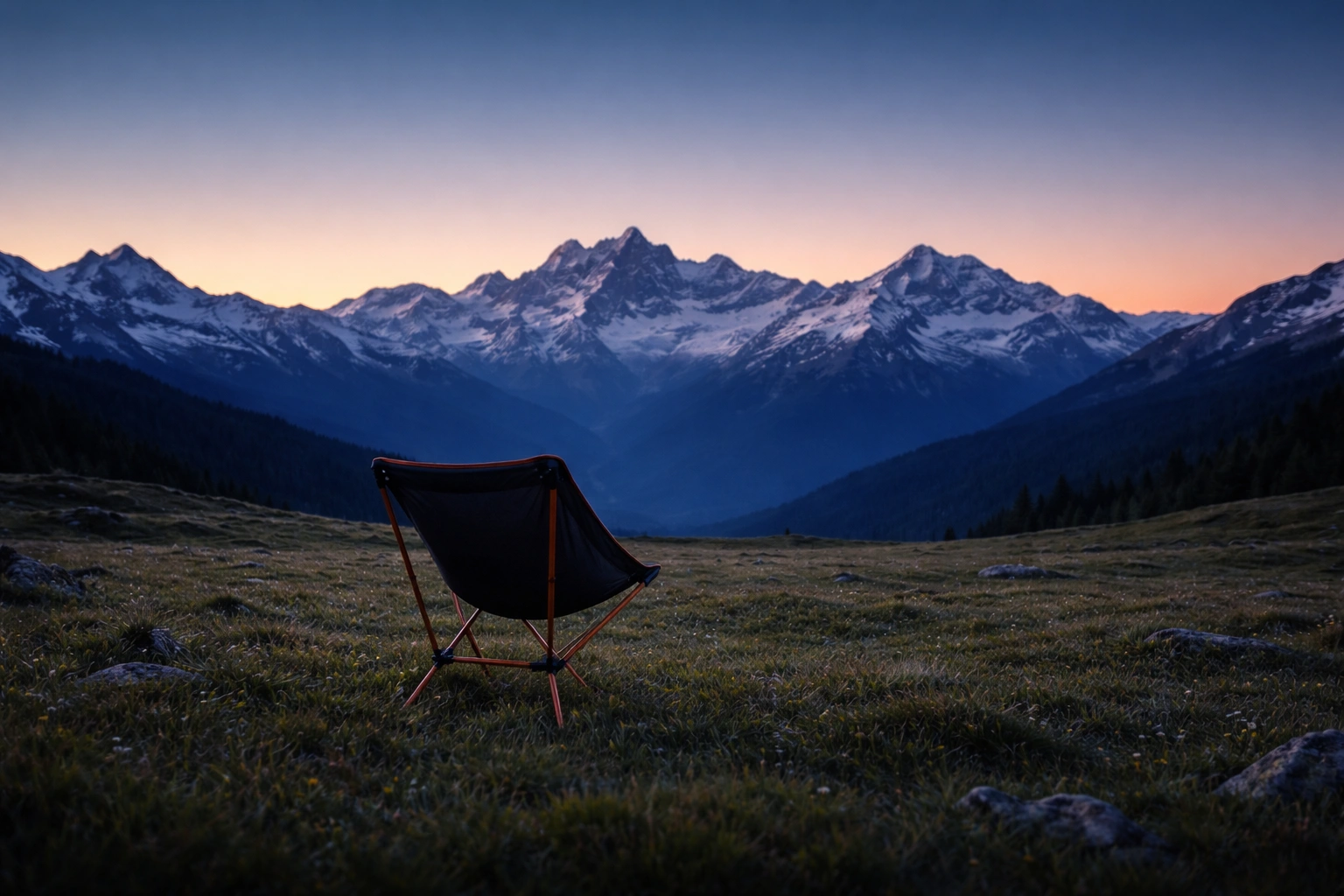 Single pole-frame ultralight camping chair set up alone on vast alpine meadow at blue hour with snow-capped peaks and deep blue orange twilight sky