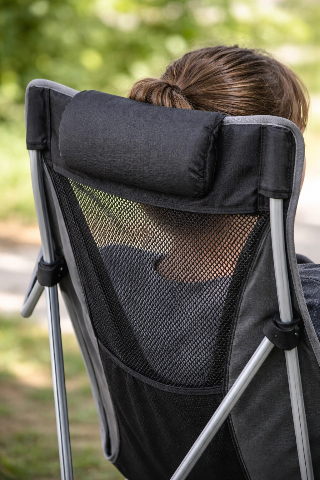 Close-up of tall camping chair backrest showing padded headrest area and breathable mesh panel below with soft daylight and green foliage bokeh