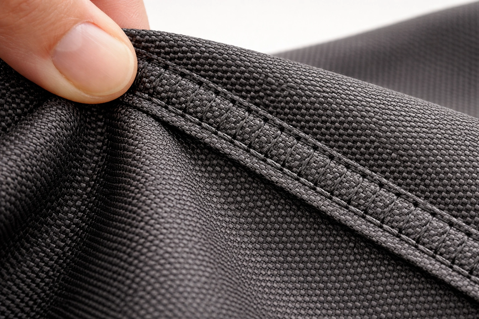 Macro photograph of thick woven 600D polyester fabric with double-stitched seams showing strength and weave pattern detail