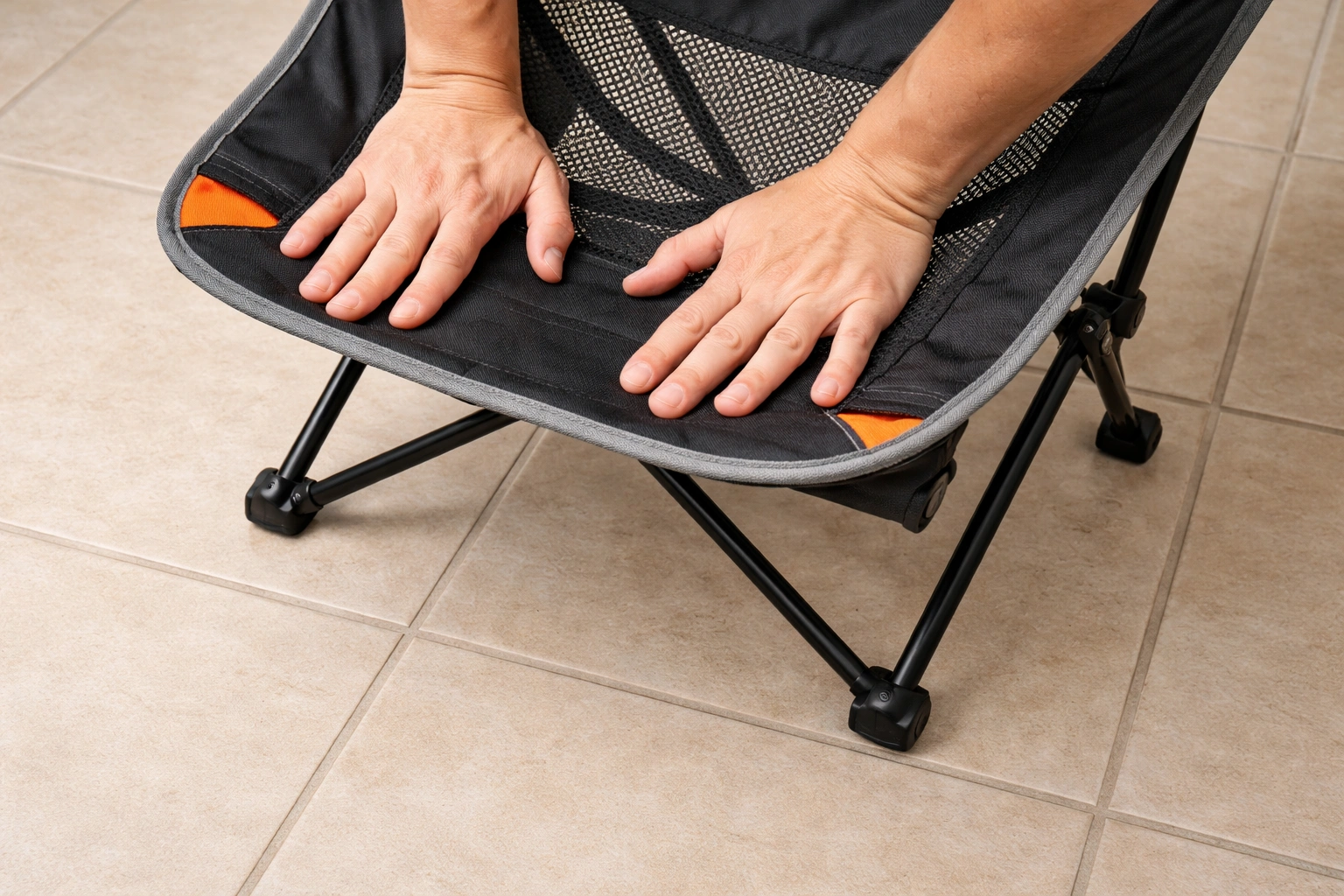 Hands pressing down on camping chair seat on flat tile floor to test for wobble with one leg lifted