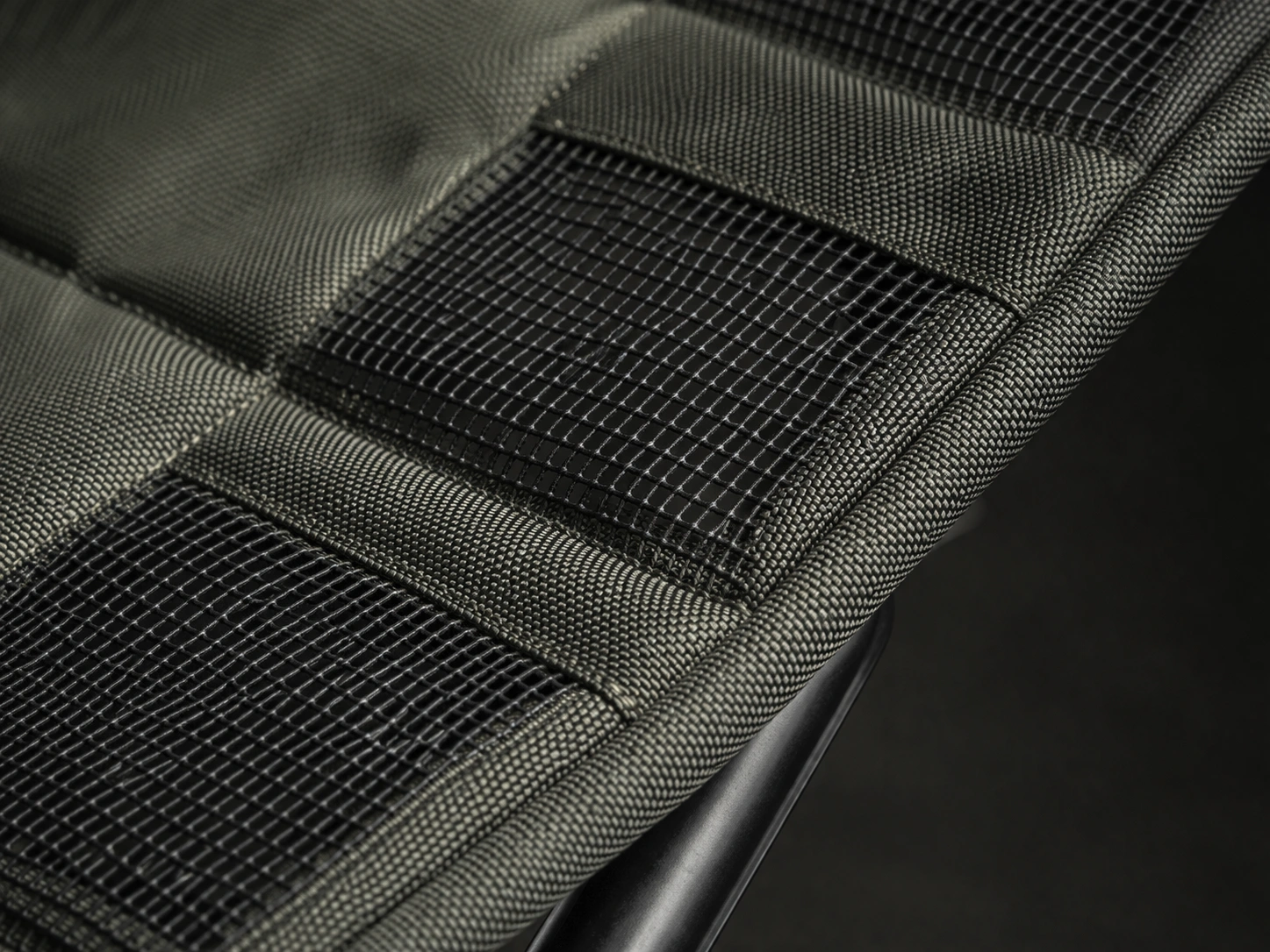 Macro of high-denier polyester fabric with integrated mesh grid pattern stretched over frame tube showing tight engineered weave with visible mesh ventilation zones in sidelight